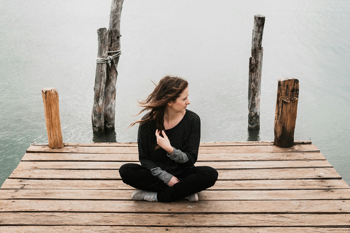 Woman sitting cross-legged on a wooden dock by the lake, reflecting peacefully—symbolising menopause mindfulness and emotional well-being.