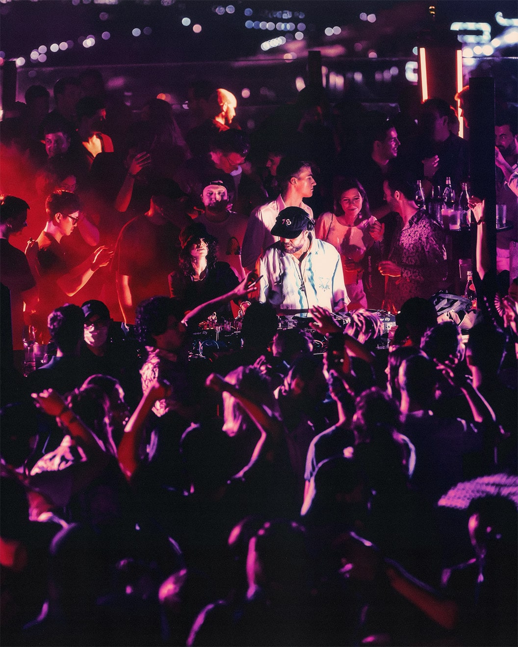 Crowd dancing at AFTER 2049 rooftop party at Marina Bay Sands during F1 Singapore 2025, with DJ performing under neon lights and city skyline in background.