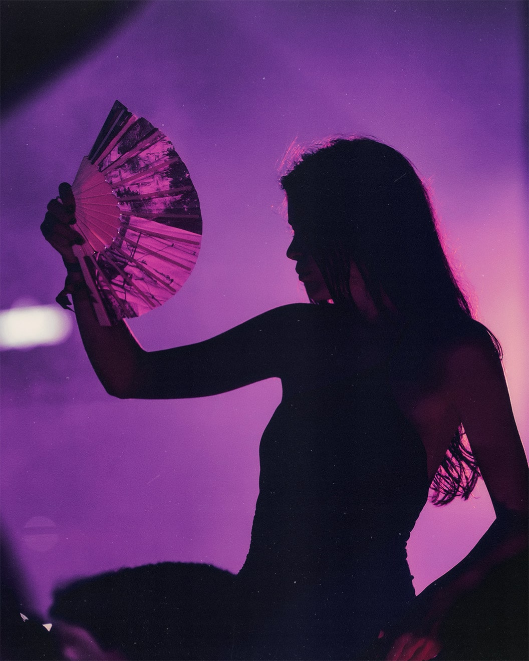 Silhouette of a woman holding a fan under purple stage lighting at AFTER 2049 party during F1 weekend in Singapore.