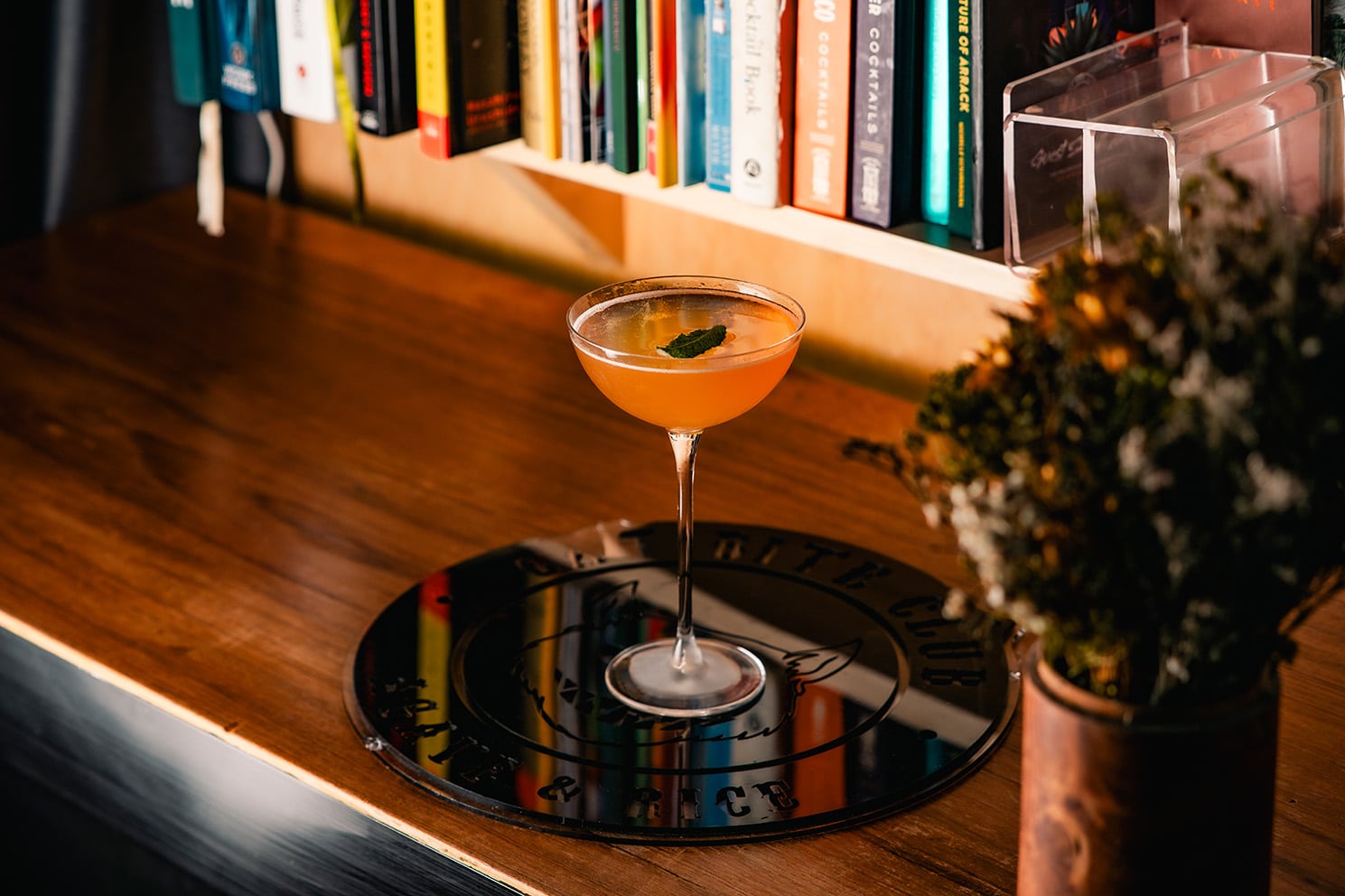 Old Cuban cocktail served at Cat Bite Club Singapore, presented in a coupe glass with fresh mint garnish, set against a curated shelf of cocktail books — modern rum and agave-focused bar in Singapore.
