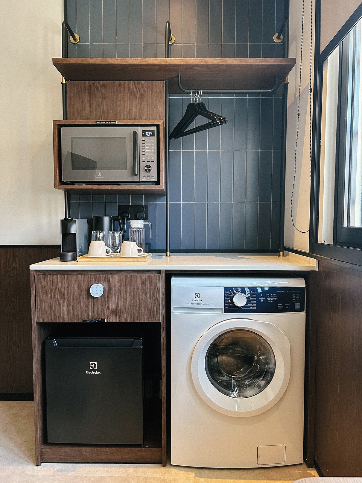 In-room amenities at Coliwoo Hotel Kampong Glam Singapore, with Electrolux washer-dryer, mini fridge, microwave, and coffee setup