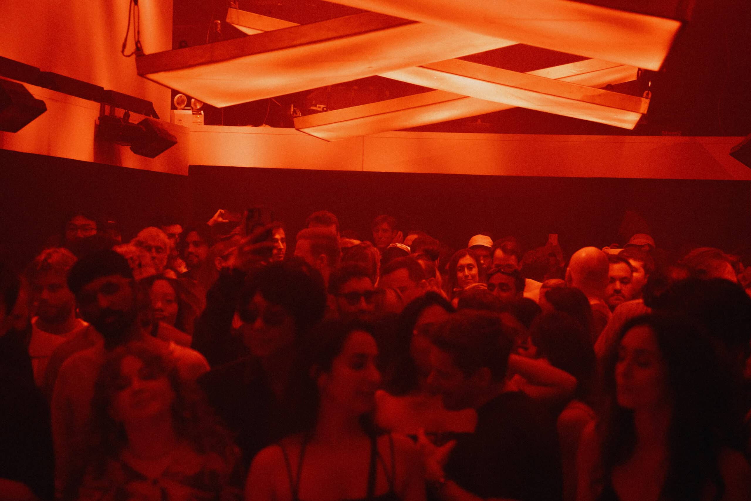 A packed dancefloor under red lighting at BEAM Bangkok in 72 Courtyard, capturing the city’s underground nightlife energy with DJs and clubgoers immersed in electronic music.