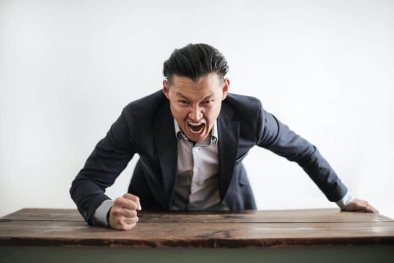A man wearing formal suit yelling and pounding the table
