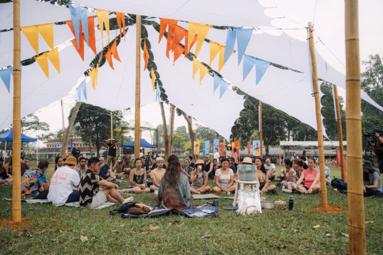 A group of people gathers in a lawn for a workshop session.
