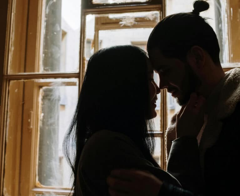 a photo of a man and woman kissing the near the window.