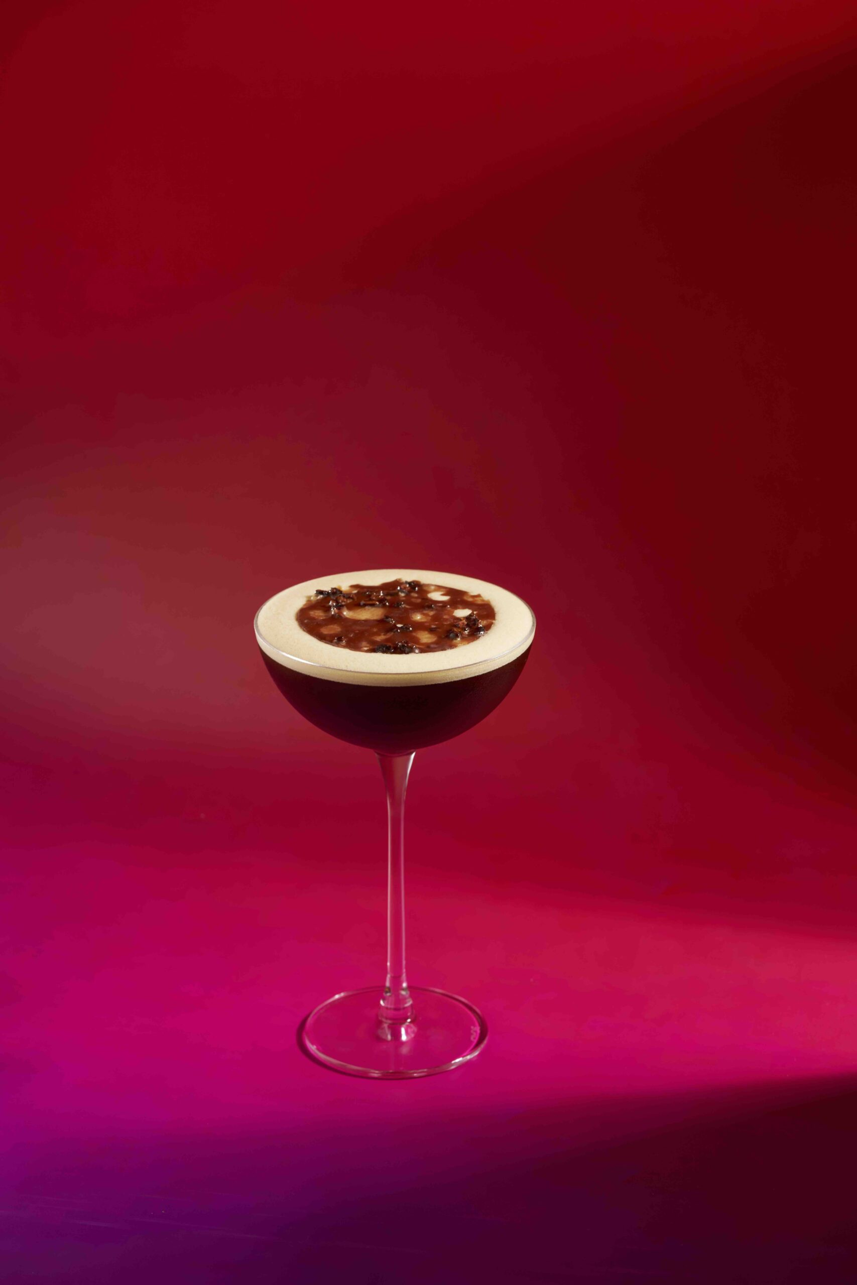 Espresso Martini from Jigger & Pony Singapore, served in a coupe glass with coffee bean garnish and frothy crema, set against a vibrant magenta-red gradient background — award-winning cocktail bar.