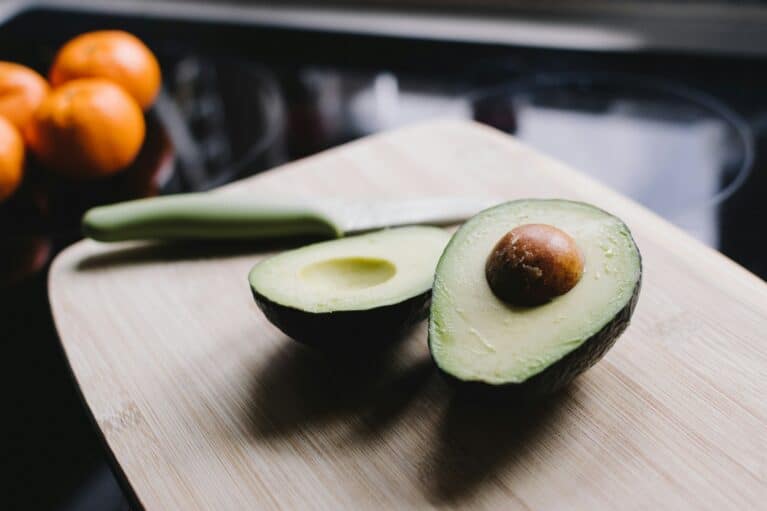 An avocado sliced in half on a wooden board.