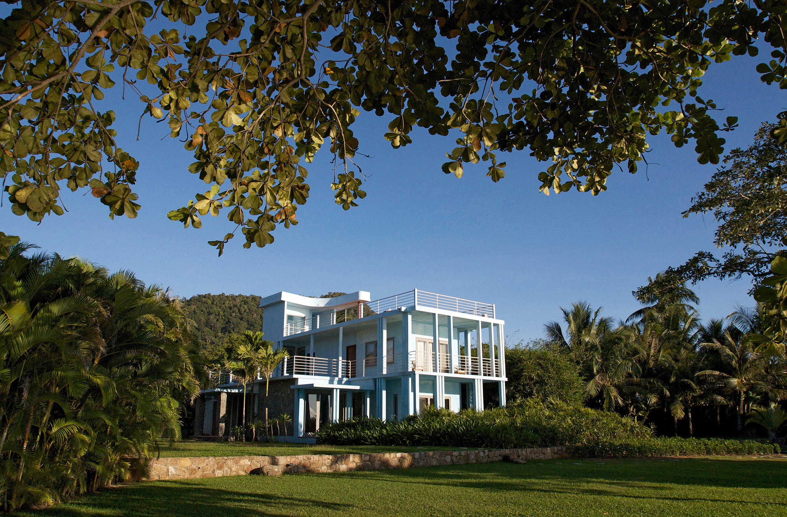 Modernist oceanfront villa at Knai Bang Chatt in Kep, Cambodia, surrounded by lush gardens and blue skies – a restored 1950s retreat blending Khmer architecture and barefoot luxury.