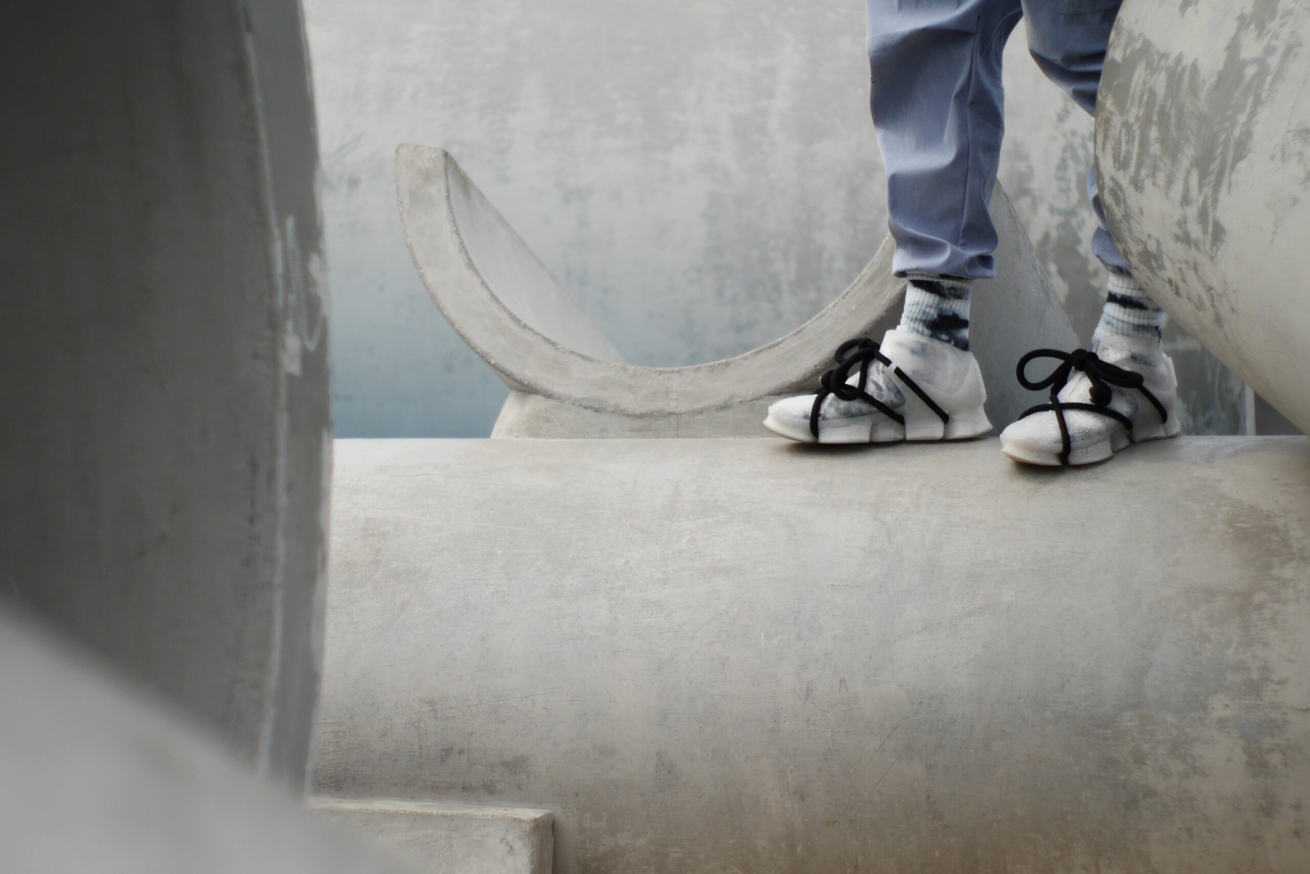 A man wearing a pair of white 3D-printed shoes standing on a concrete cylinder