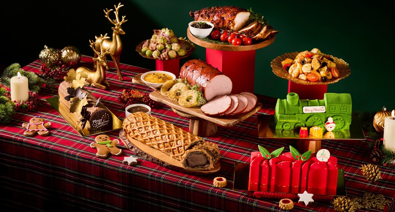 Princess Terrace Christmas takeaway spread featuring beef Wellington, pineapple-glazed ham, roasted turkey breast, festive pasta salad, chocolate log cakes, and vibrant green and red holiday desserts on a tartan table setting.