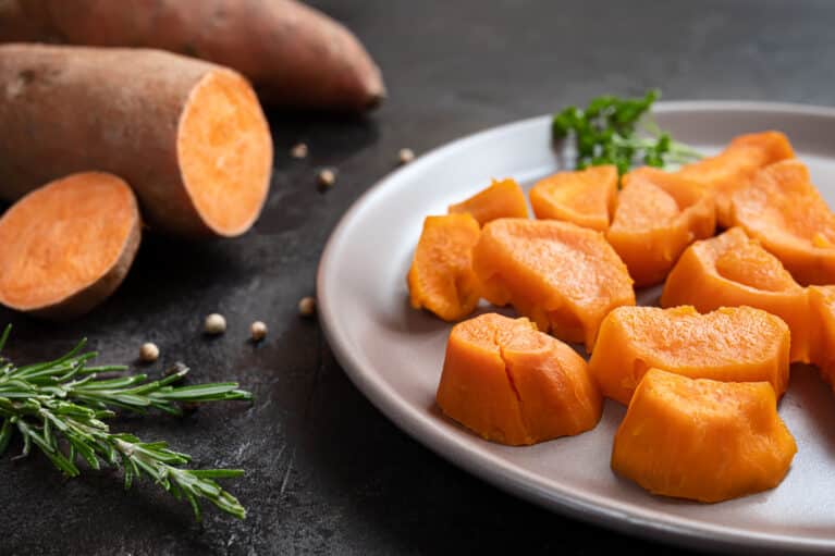 Roasted sweet potatoes and raw yam on a dark table 