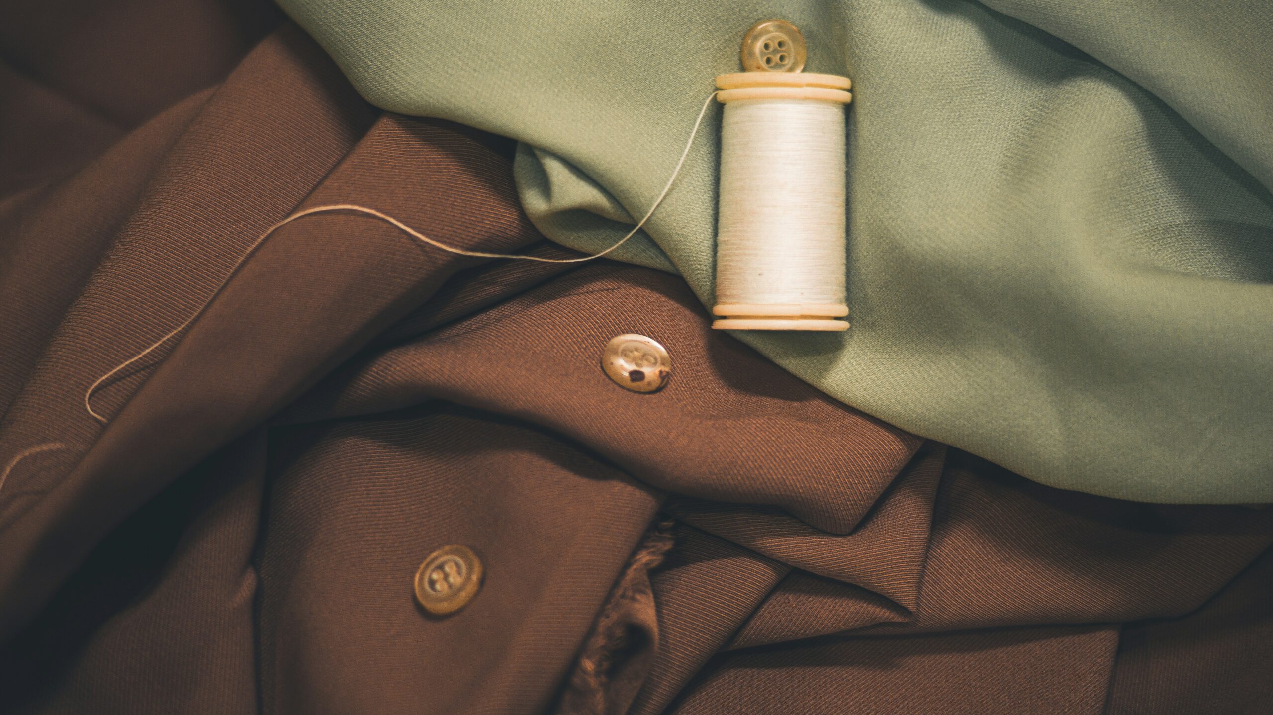 Green and brown textile fabrics, a thread and buttons.